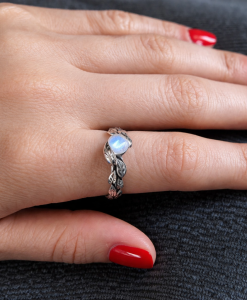 White gold leaf engagement ring with black rhodium detailing, featuring a glowing rainbow moonstone center stone, nature-inspired handmade design, delicate organic band, unique alternative bridal ring