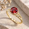 Nature-inspired gold engagement ring with a cushion-cut red ruby and twisted rope band, photographed on warm natural stone.