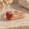 Nature-inspired gold engagement ring with a cushion-cut red ruby and twisted rope band, photographed on warm natural stone.